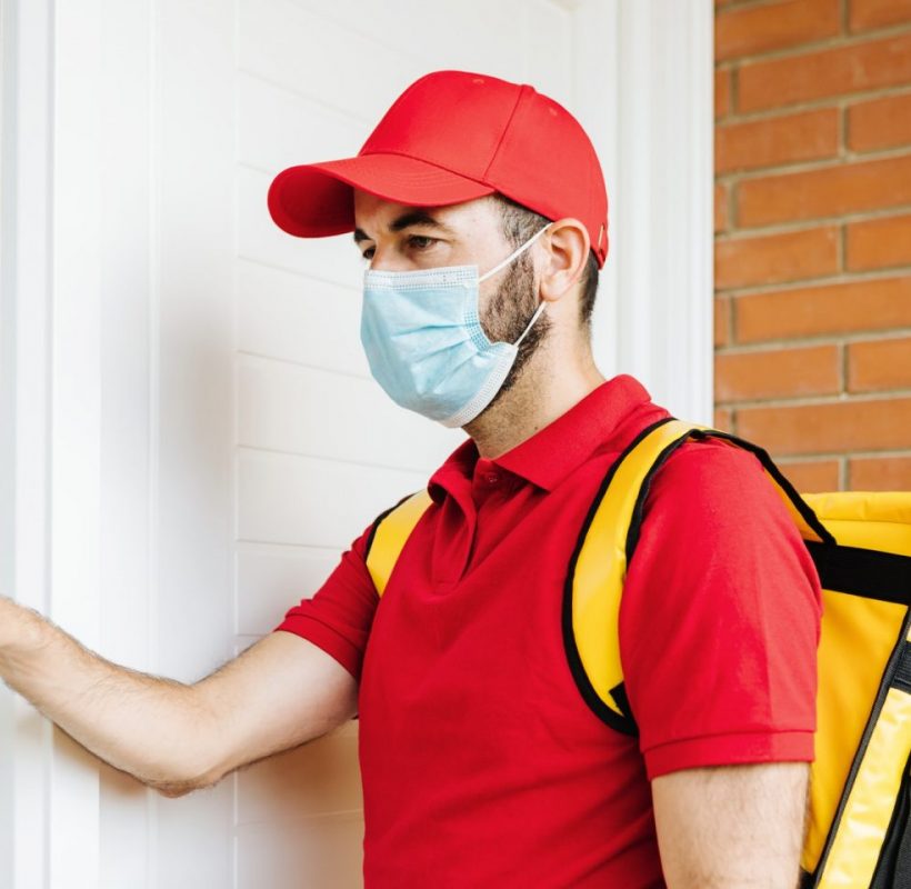 Young hispanic delivery food man in face mask ringing the doorbell - Food delivery concept